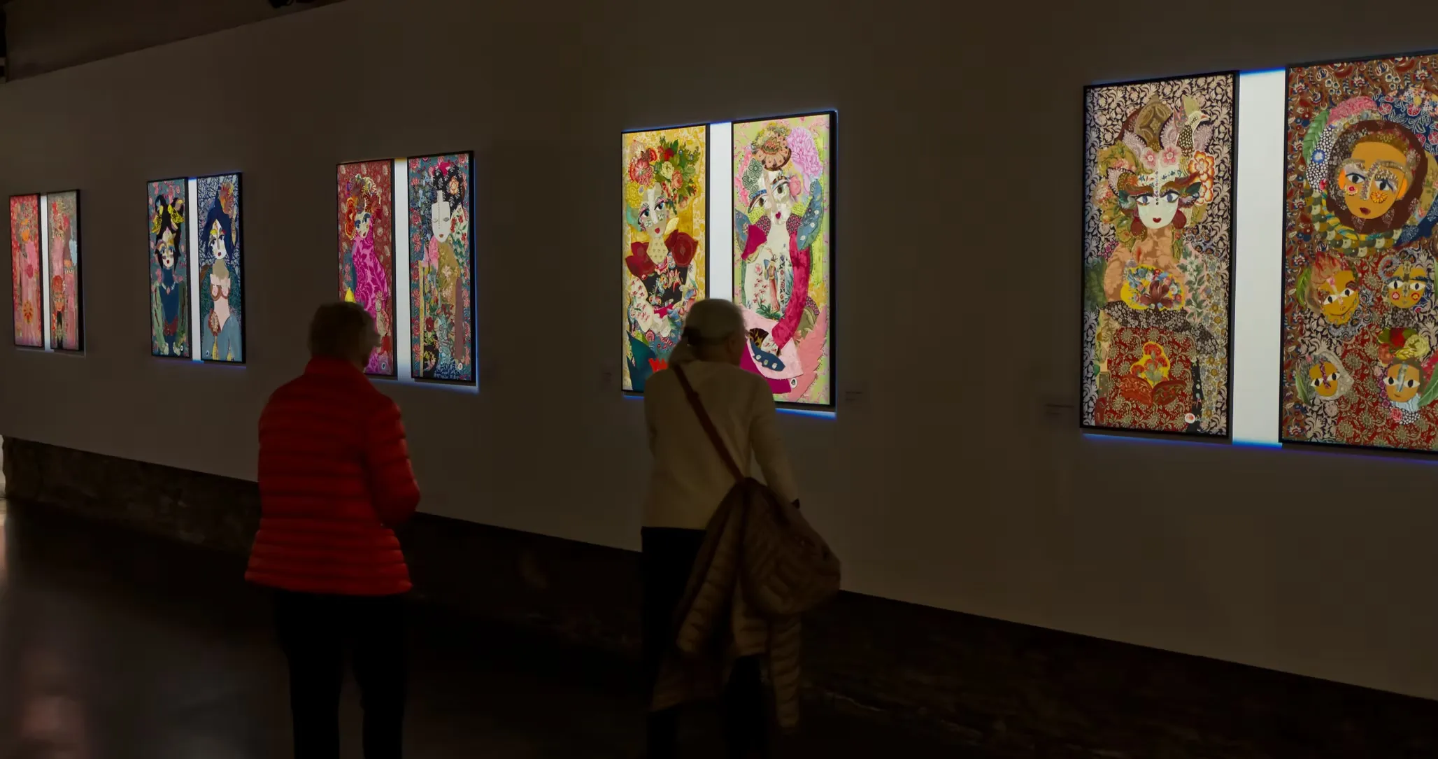 Visiteur en manteau rouge face à plusieurs portraits textiles accrochés, Katherine Roumanoff, exposition Trélazé Angers